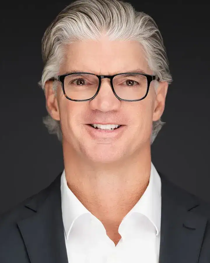 Tampa professional headshot of a man with gray hair and glasses in a dark suit on a dark backdrop